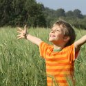 Young child in a field with arms oustretched in joy