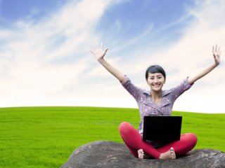 Young woman with laptop outside with arms raised